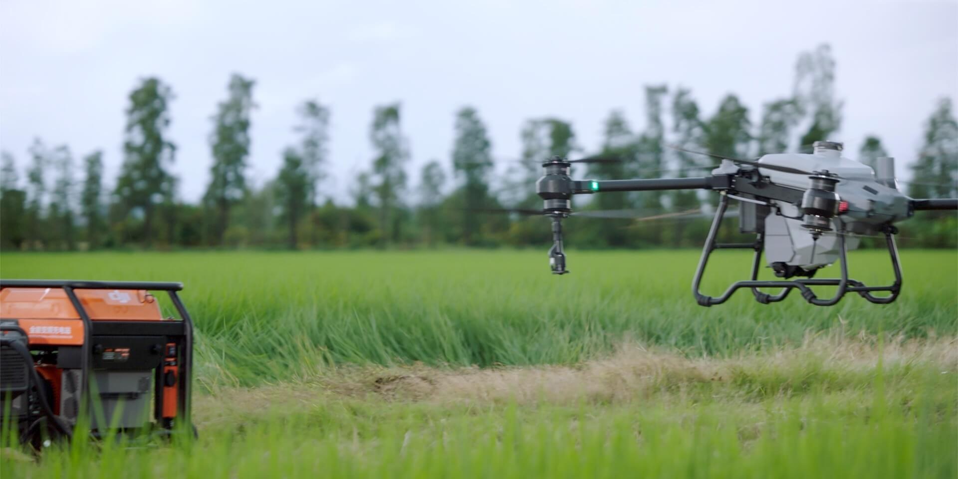 Praca z agregatem DJI Agras T25P nad polem, w tle agregat do ładowania
