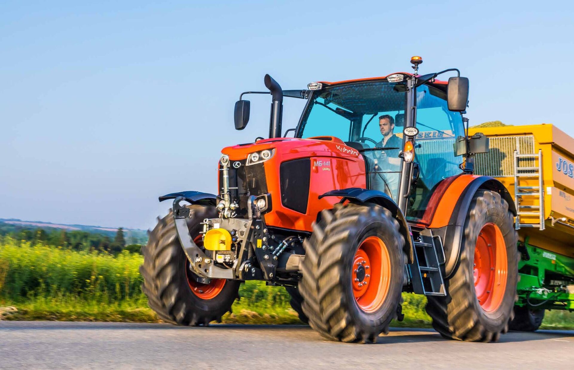 Ciągnik Kubota M6001 Utility z przyczepą na drodze, widok z przodu