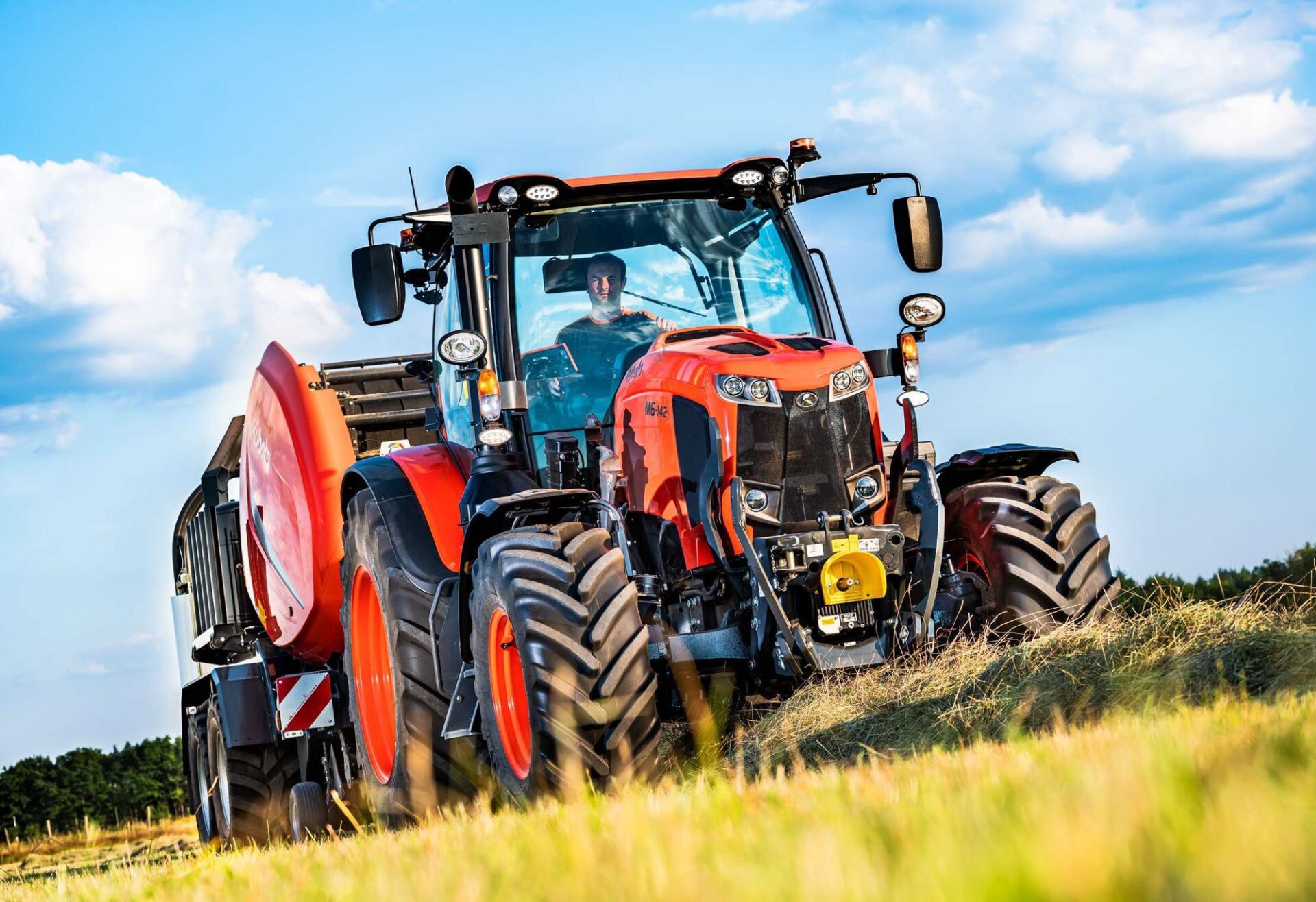 Ciągnik Kubota M6002 z prasą zwijającą na łące, widok z przodu