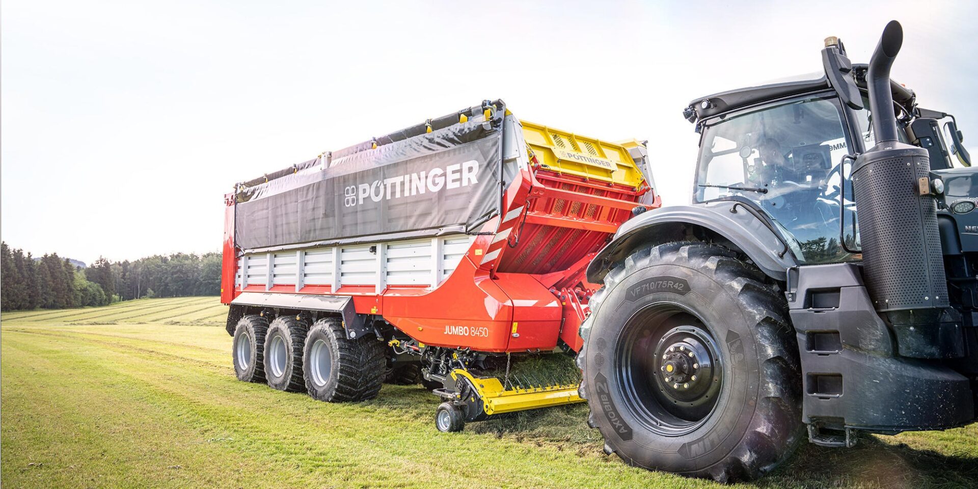 Przyczepa samozbierająca Pöttinger JUMBO 8000 z podwoziem tridem i ciągnikiem na łące