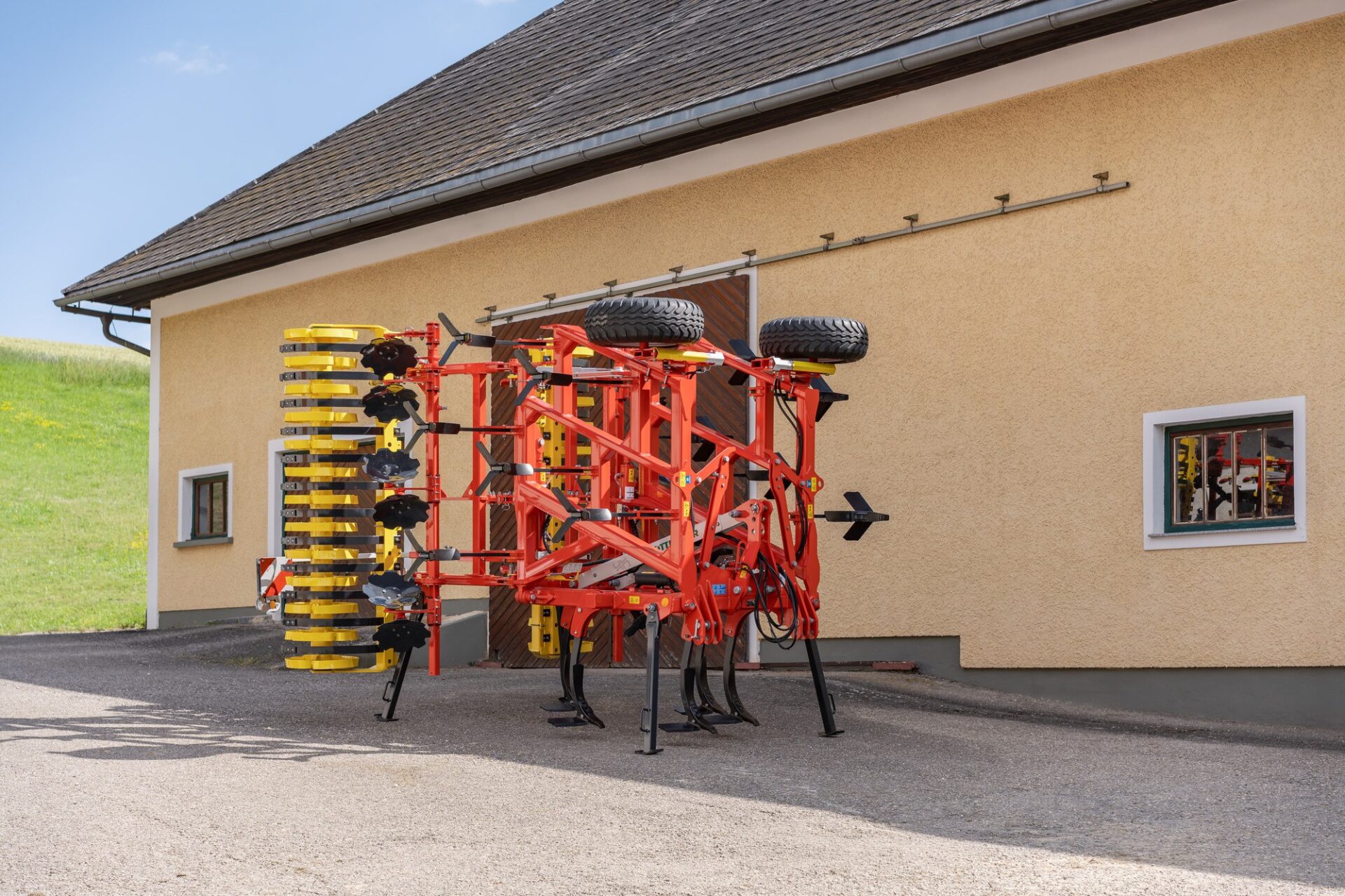 SYNKRO V 5031 – pozycja transportowa Pöttinger SYNKRO V 5031 złożony do transportu na podporach przy budynku gospodarstwa