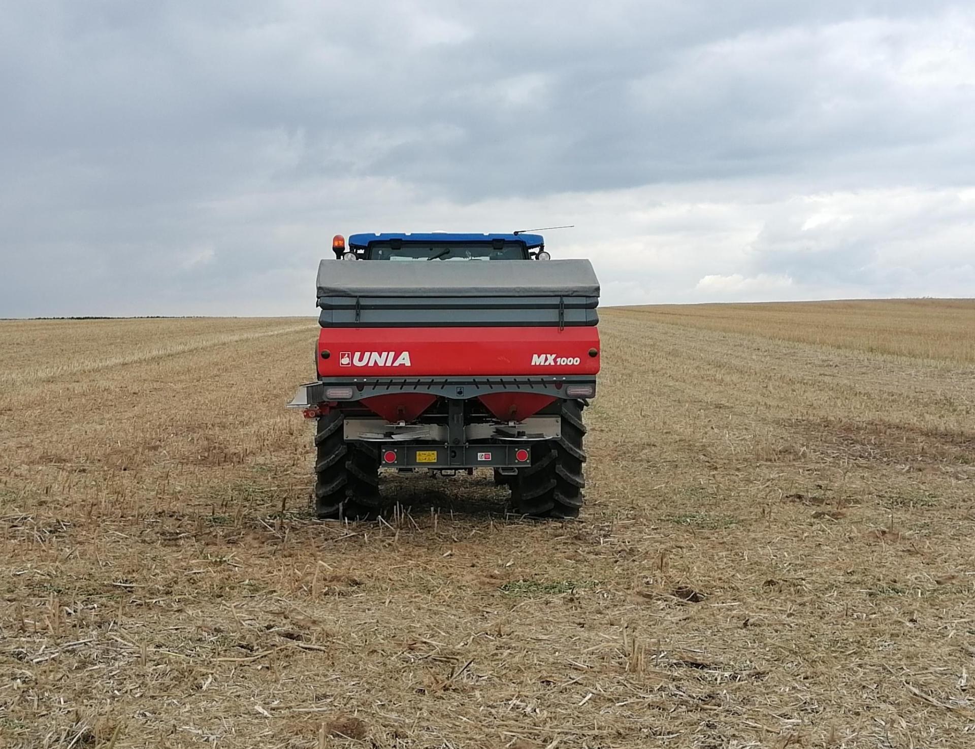 MX na polu Rozsiewacz UNIA MX na ciągniku na ściernisku, widok z tyłu